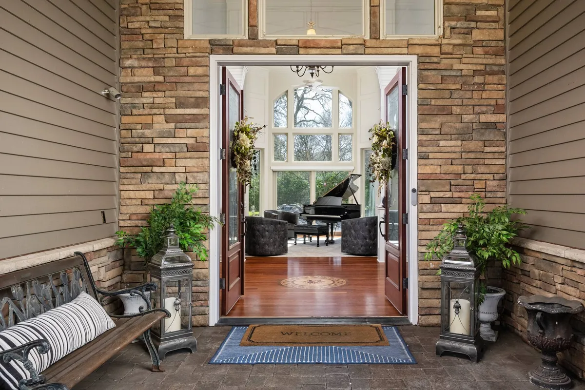 A dramatic foyer with double doors opening onto a grand piano, decorative plants, and an intimate seating area. The view captures the home's welcoming first impression and musical centerpiece.