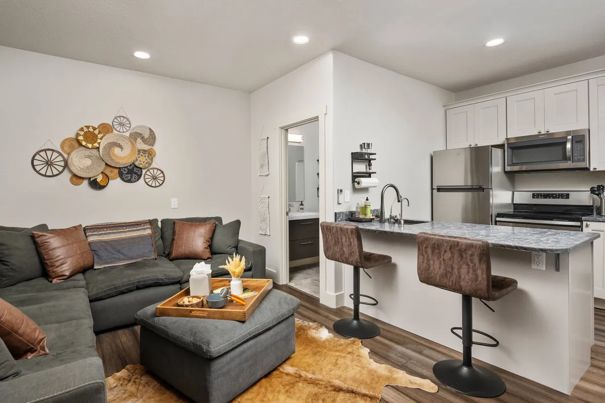 A cozy, open-plan area combining a sofa, kitchen island with bar stools, and decorative wall art, creating a multi-functional setting. The scene is ideal for casual gatherings, morning breakfasts, or prepping for a day outdoors.