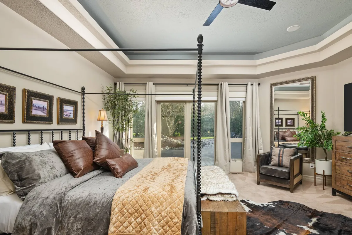 A serene bedroom featuring a canopy bed with plush throws, a bamboo plant, a large mirror, and a wooden dresser. The space is bright with natural light, inviting relaxation or quiet moments overlooking the surrounding scenery.