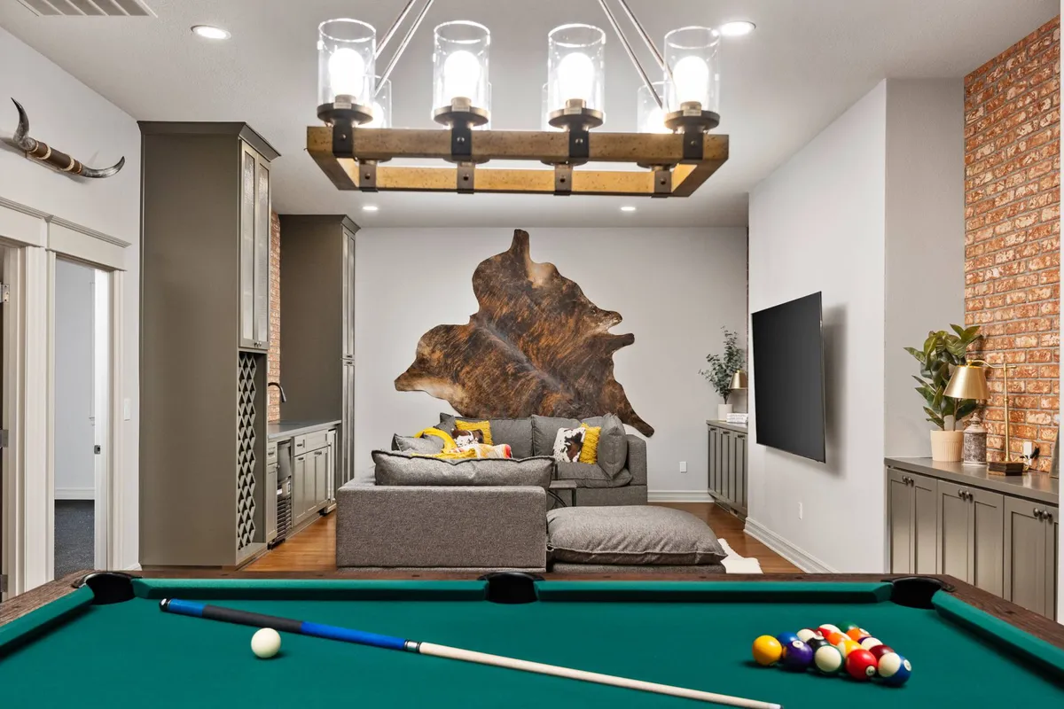 The image features a relaxed entertainment area with a pool table, a comfortable sofa adorned with colorful cushions, a wood feature wall, and a chandelier. The setting encourages friendly competition and social bonding, ideal for group retreats and team-building activities.