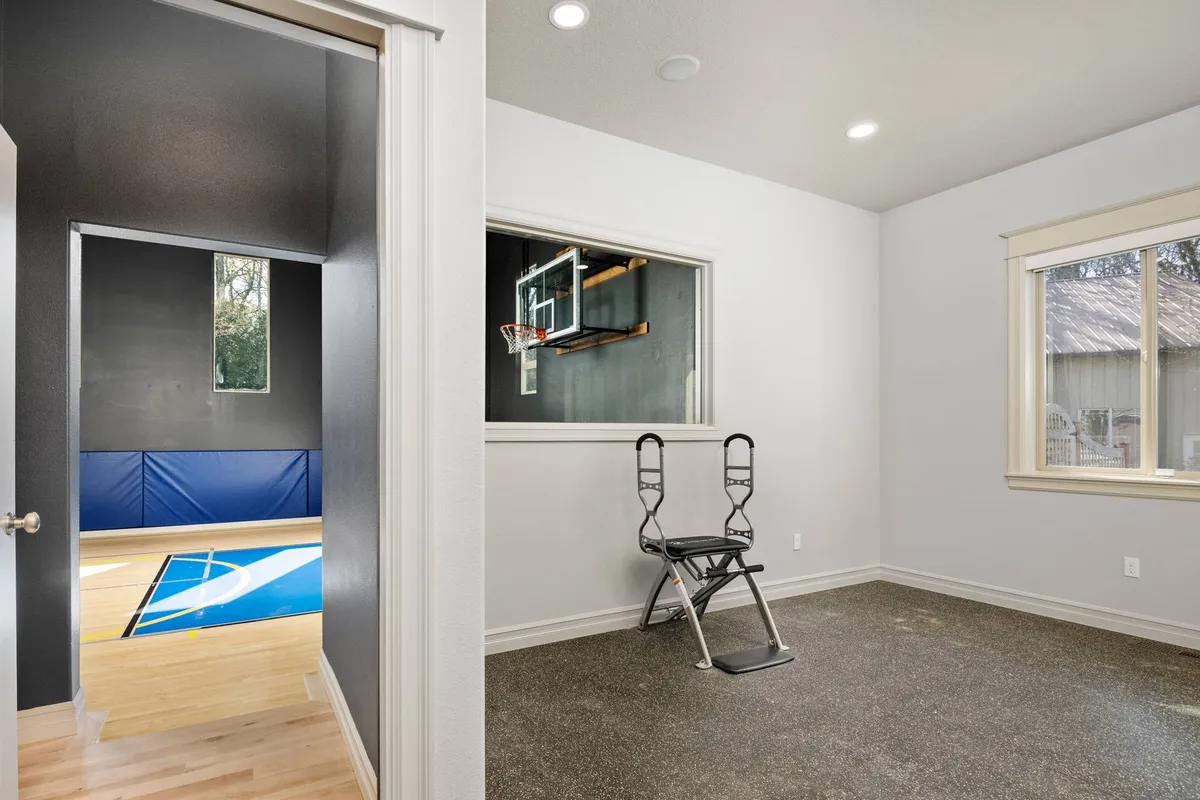 A versatile space featuring a basketball hoop for shooting practice, an exercise chair, and a large window that brings in ample light. Designed for both active play and personal workouts, the setting invites movement and fitness.