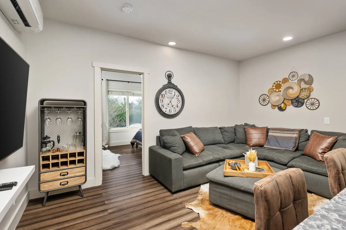 This image features a spacious living room with a large sectional sofa, decorative wall art, a prominent clock, and a coffee table with tasteful decor. The layout suggests a welcoming and communal environment, ideal for relaxing after outdoor adventures or spending time with pets inside.