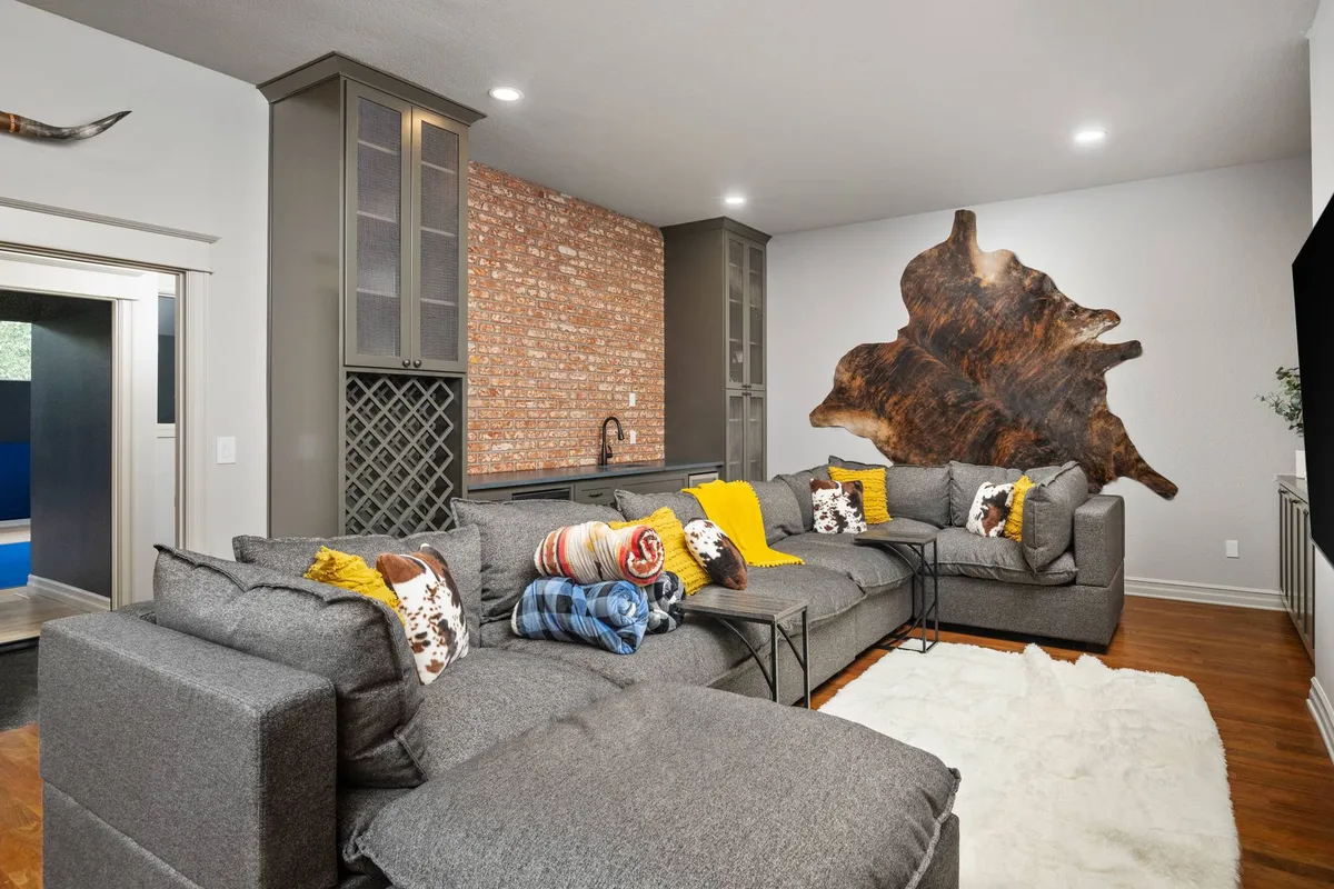 A warm-toned living room with a large sectional sofa and textured accent wall, featuring a prominent wooden art piece. The inviting space suggests comfort and togetherness, ideal for gatherings or relaxing after outdoor activities.