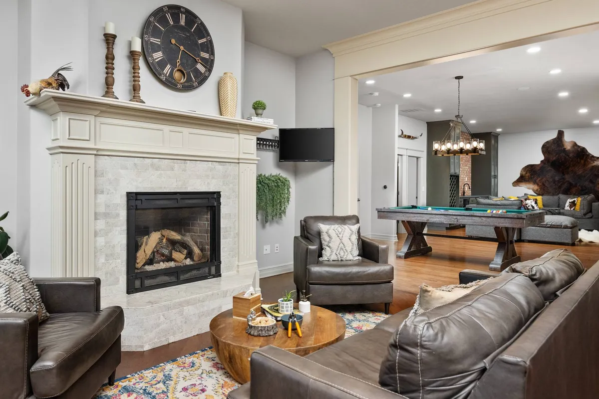 A spacious family/living room featuring sectional seating, a glowing fireplace, a custom pool table, and a stylish coffee table—all arranged for socializing and relaxation.
