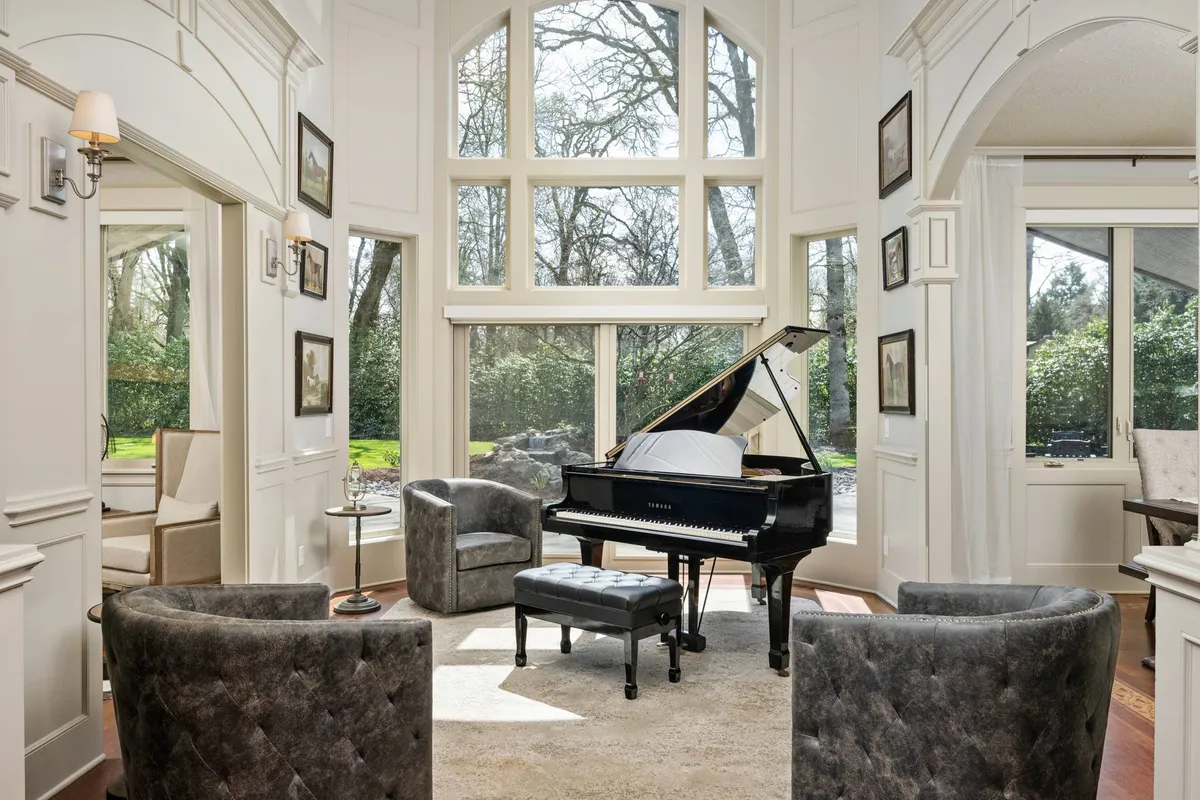 A sophisticated sitting area featuring a grand piano as the centerpiece, surrounded by plush armchairs, large windows that let in ample sunlight, and elegant decorative wall frames. The ambiance is refined yet inviting, setting the tone for gatherings and musical moments.